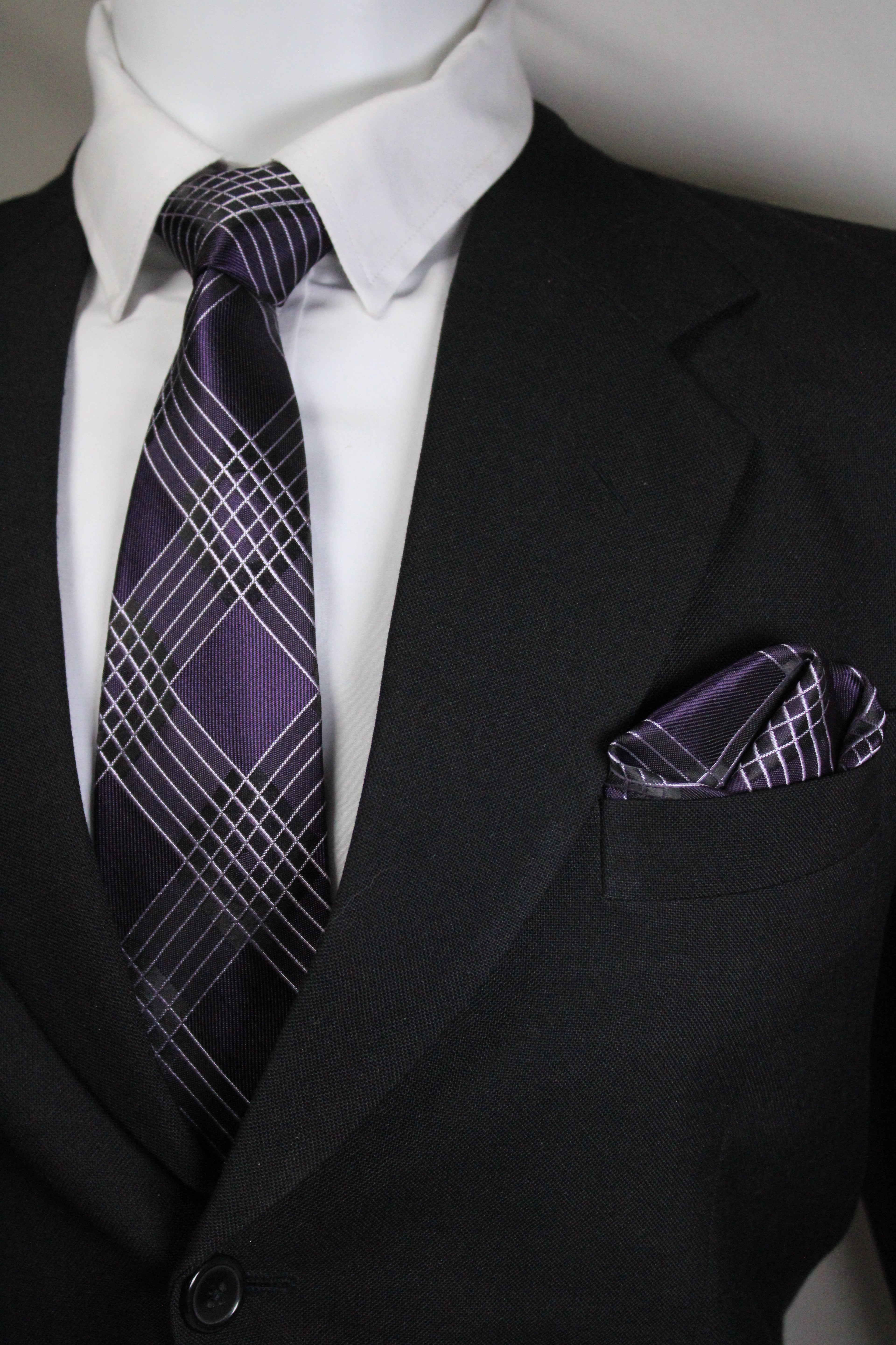 Close-up of a black suit with a white shirt and purple plaid tie tie benon