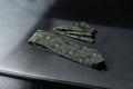 A green and black paisley tie and pocket square set laid out on a dark surface.
