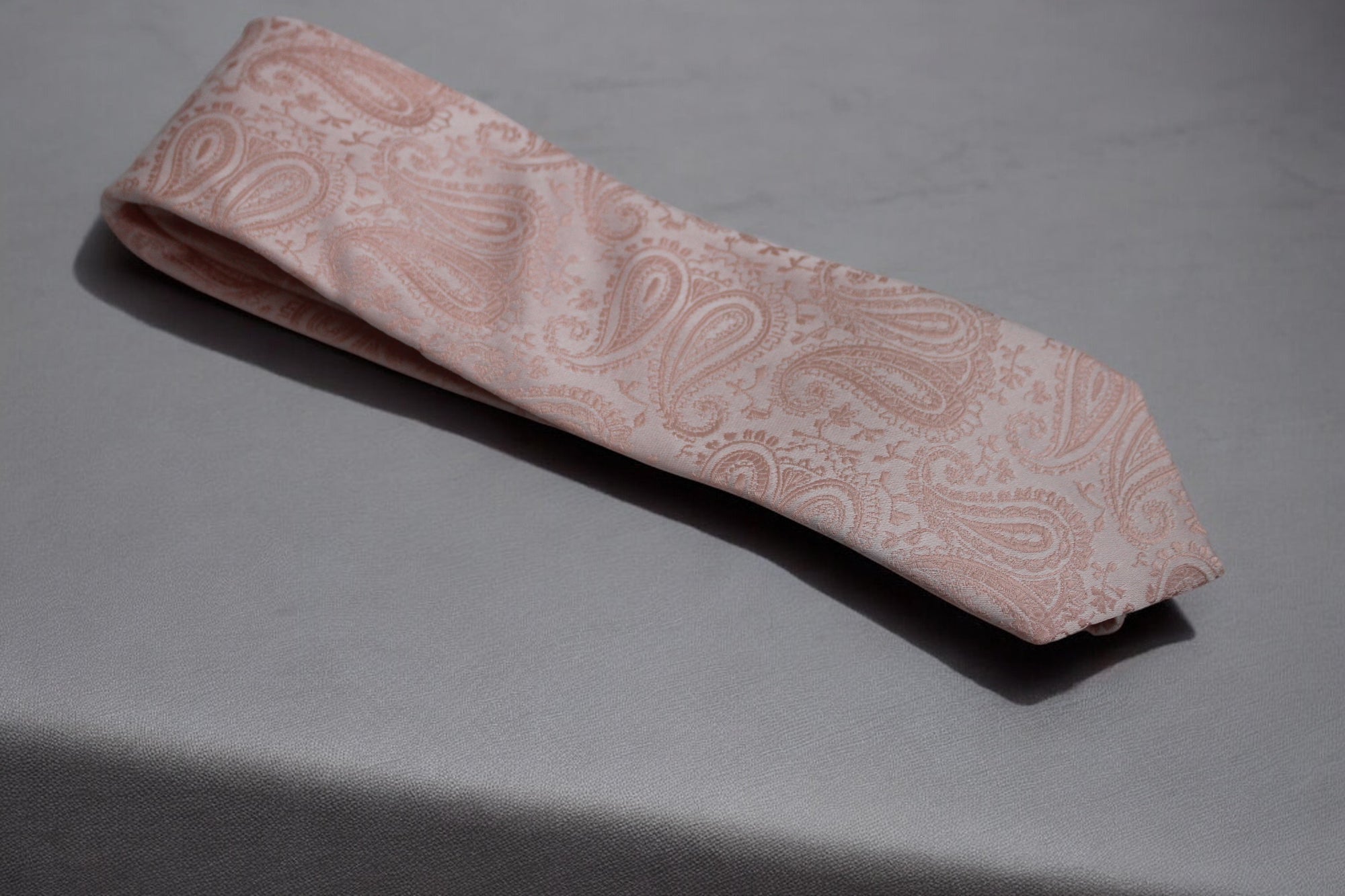 A light pink necktie with a self paisley pattern, displayed on a flat surface.