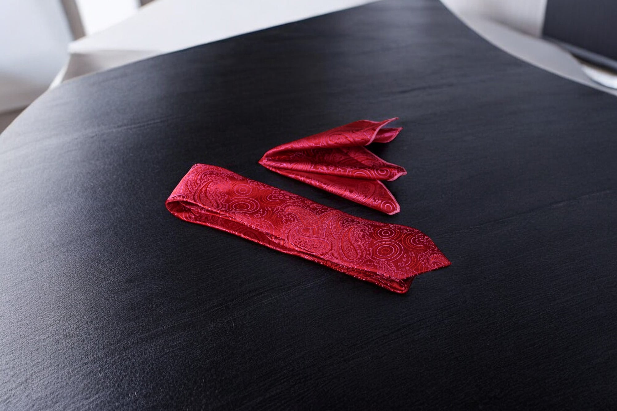 A red paisley necktie and pocket square set laid out on a surface.