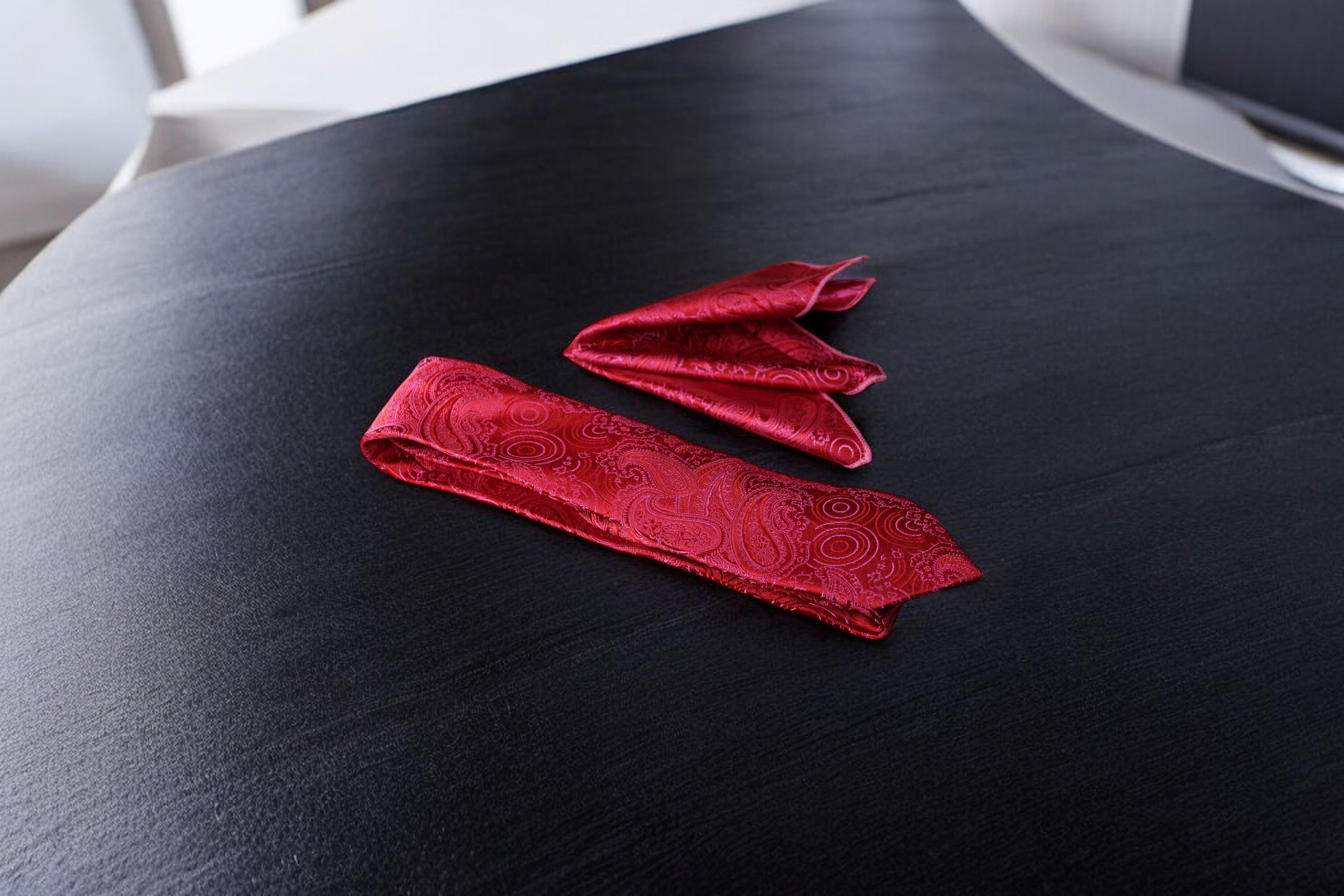 A red paisley necktie and pocket square set laid out on a surface.