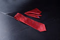 A red necktie with a pattern and a matching pocket square placed on a dark surface.