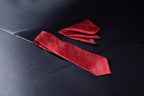 A red necktie with a pattern and a matching pocket square placed on a dark surface.
