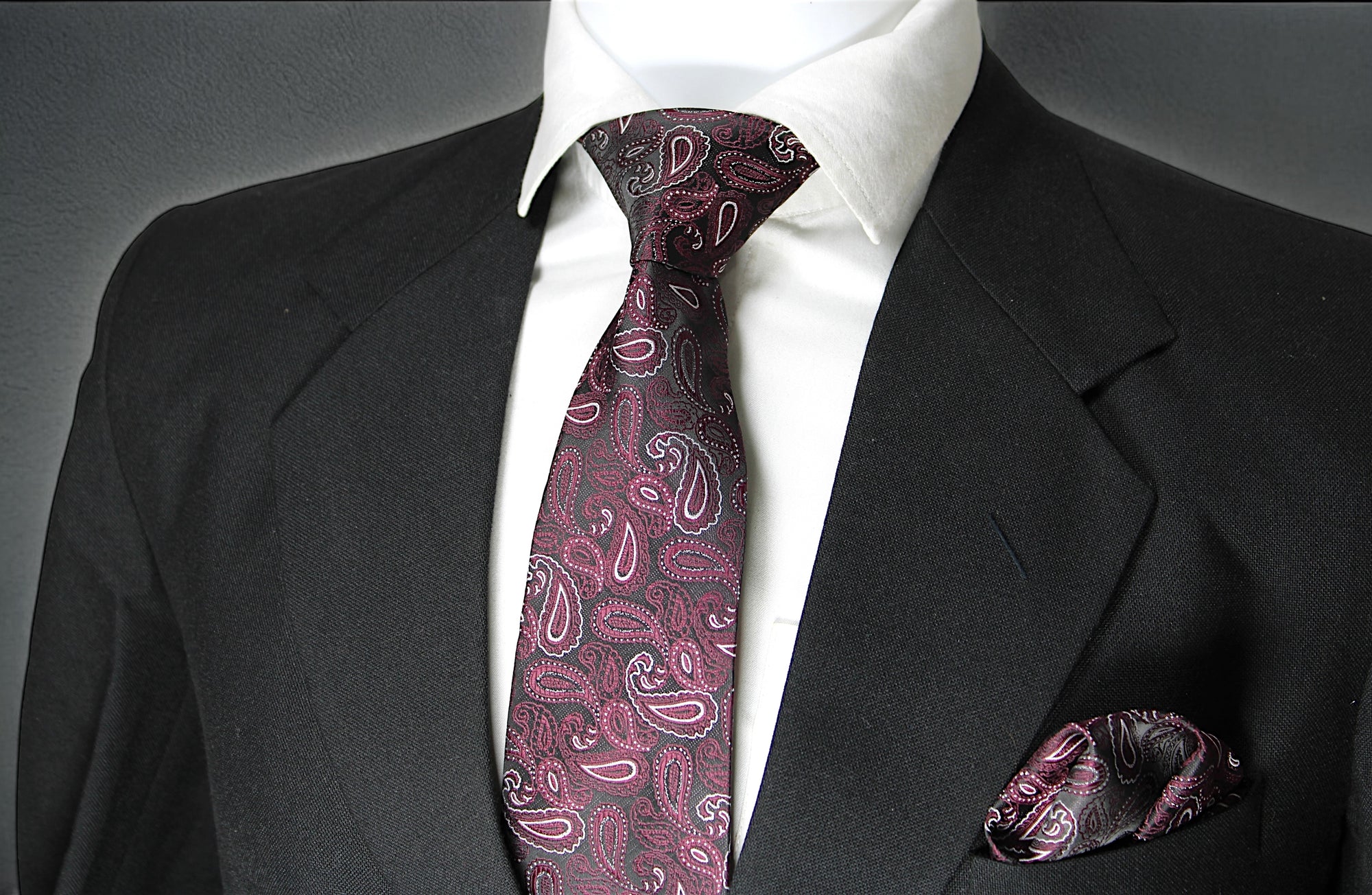 A set comprising a wine paisley tie and a matching pocket square, displayed on a mannequin wearing a black suit and a white shirt.
