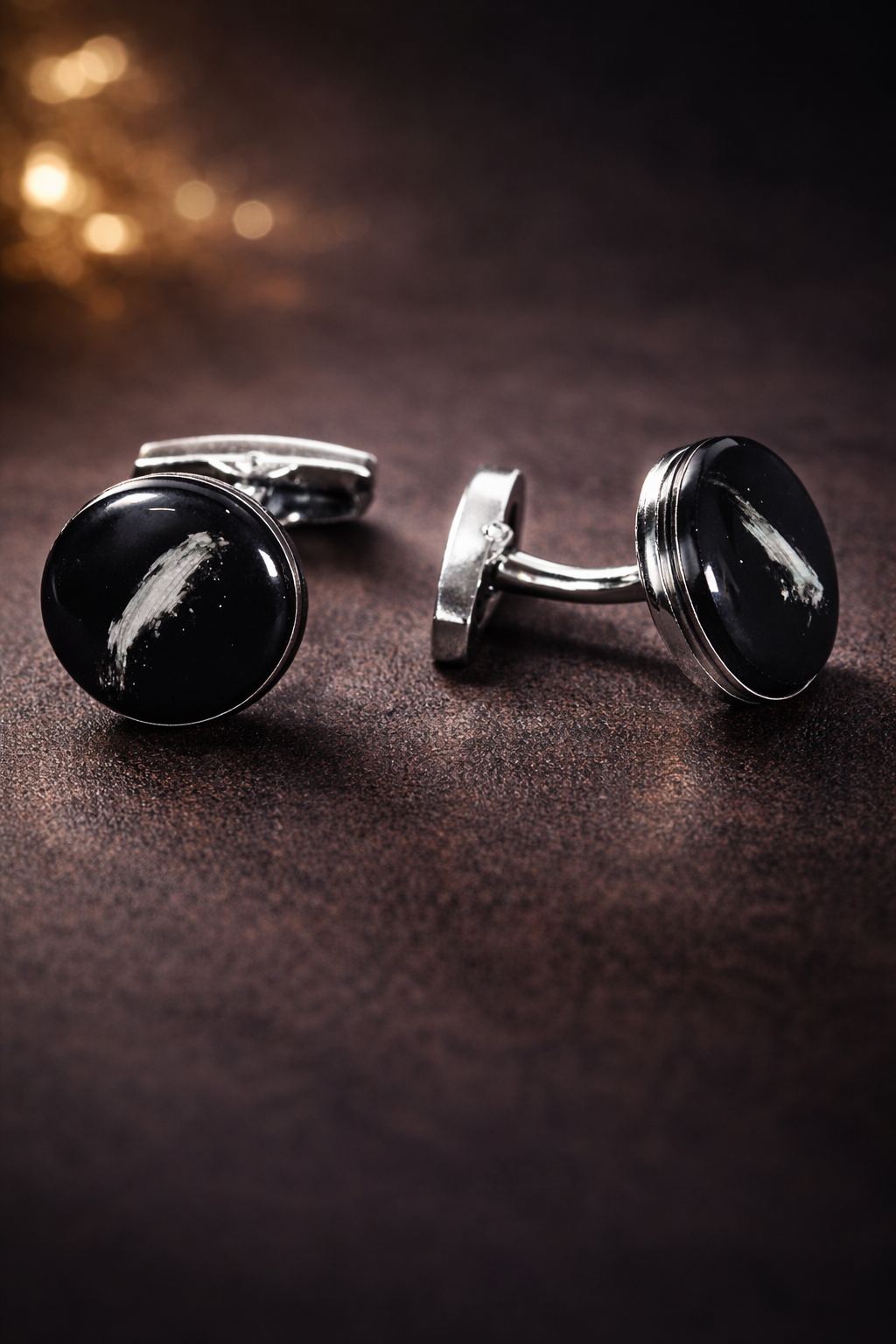 Black cufflinks with silver accents on a dark brown surface