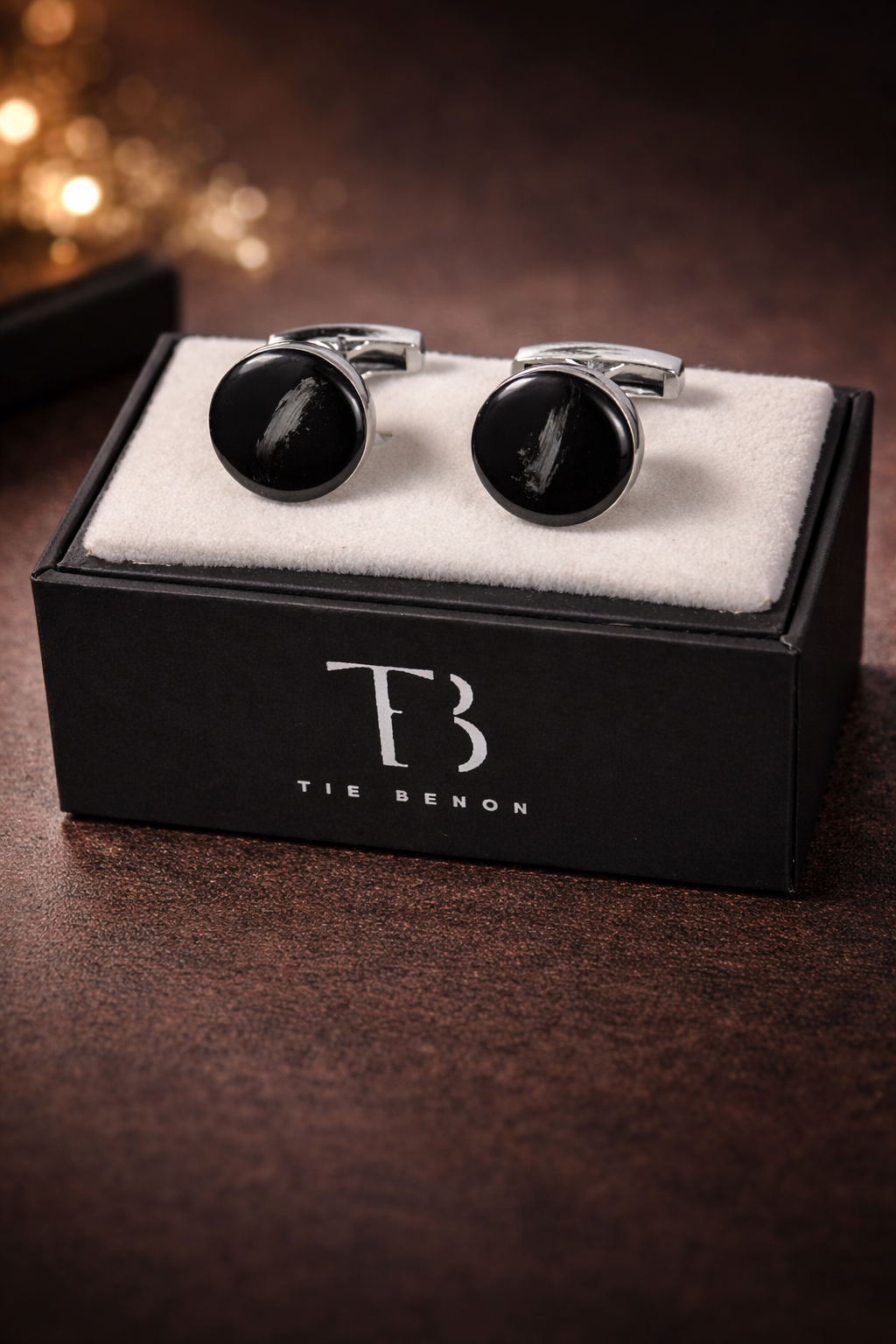 Black cufflinks on a box with 'TB' branding on a dark background
