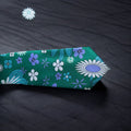 An emerald green necktie with a floral pattern, displayed on a textured background.