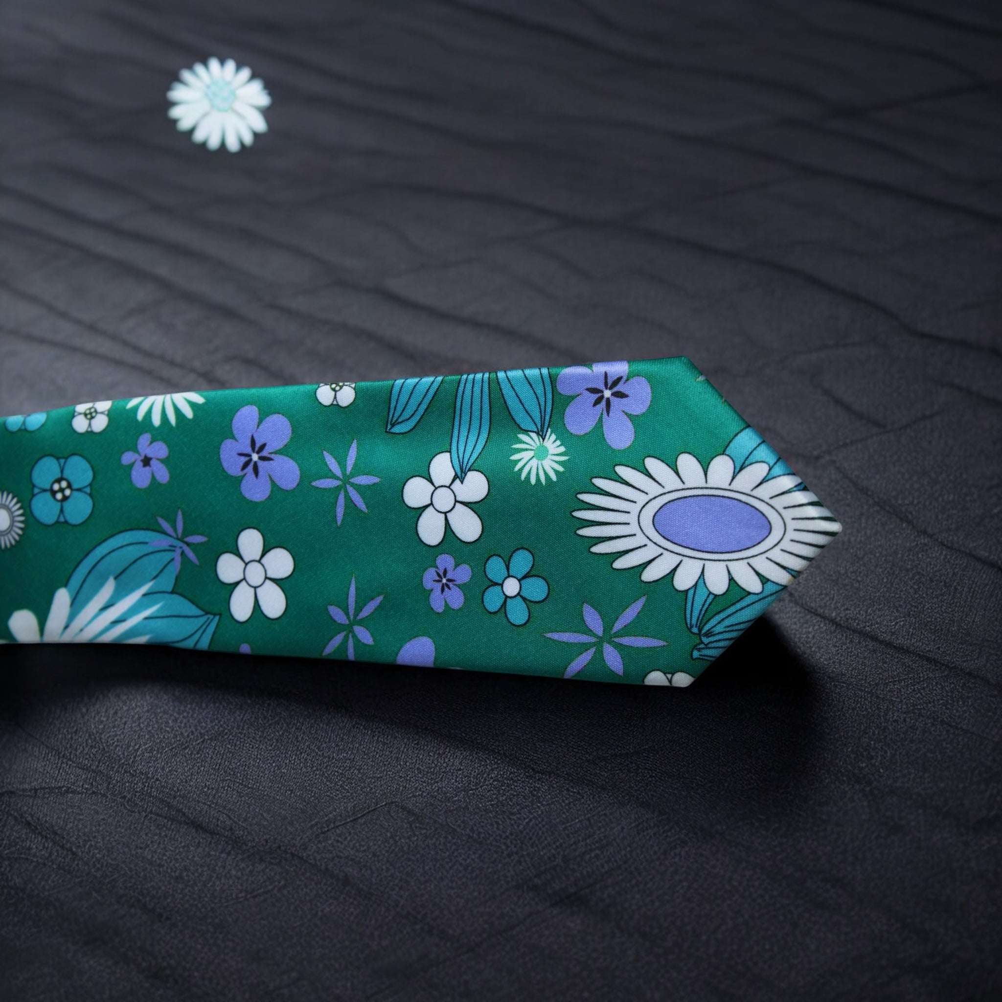An emerald green necktie with a floral pattern, displayed on a textured background.