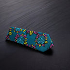 A dark sea green necktie with a floral pattern in pink and yellow, displayed on a dark background.