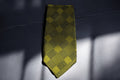 A golden plaid tie laid out on a surface, displaying a pattern of yellow and black lines.