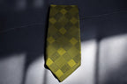 A golden plaid tie laid out on a surface, displaying a pattern of yellow and black lines.