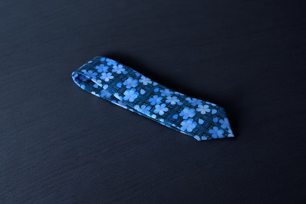 A blue necktie with a geometric pattern laid out flat on a dark background.