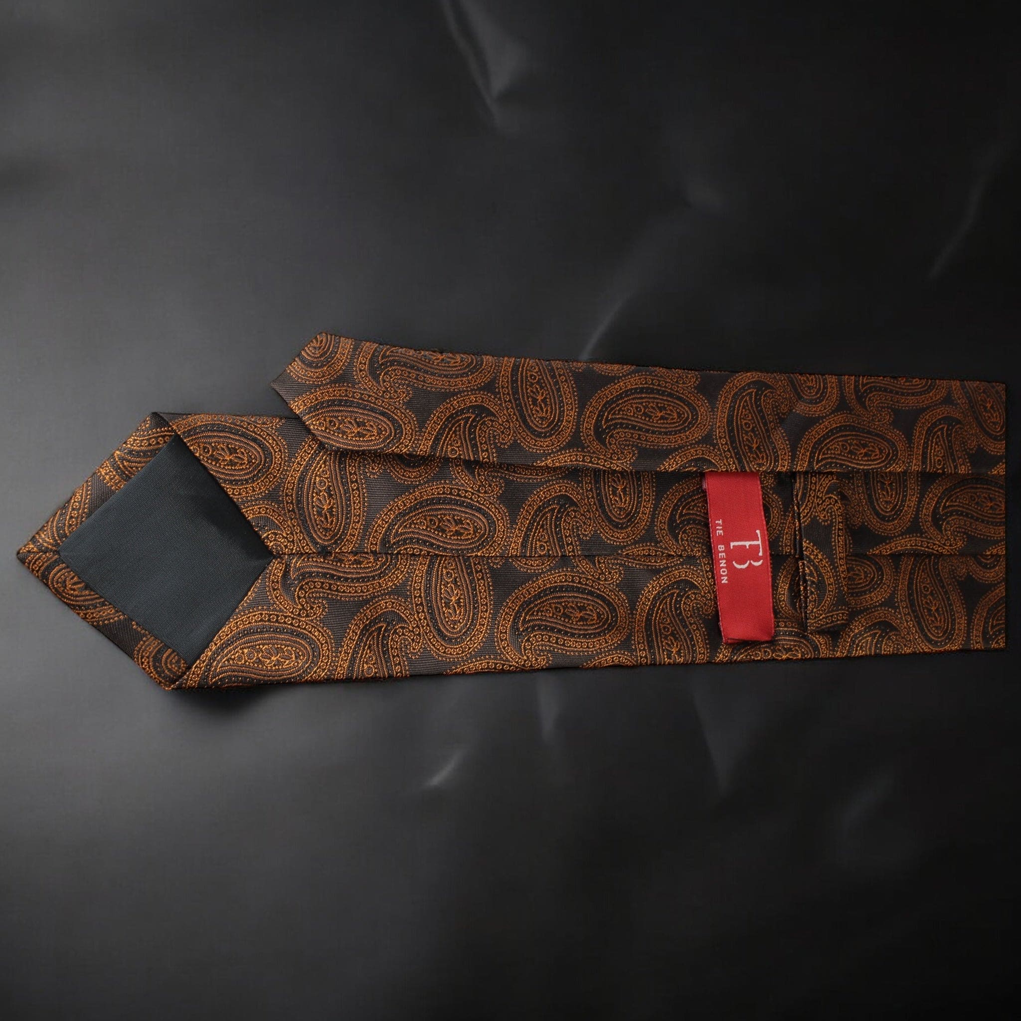 Brown paisley patterned tie with a red tag on a black background