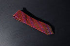 A luxurious red microsilk tie with a vibrant geometric pattern laid out on a dark surface.