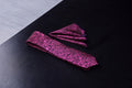 A set of magenta and black floral tie and pocket square laid out on a dark surface.