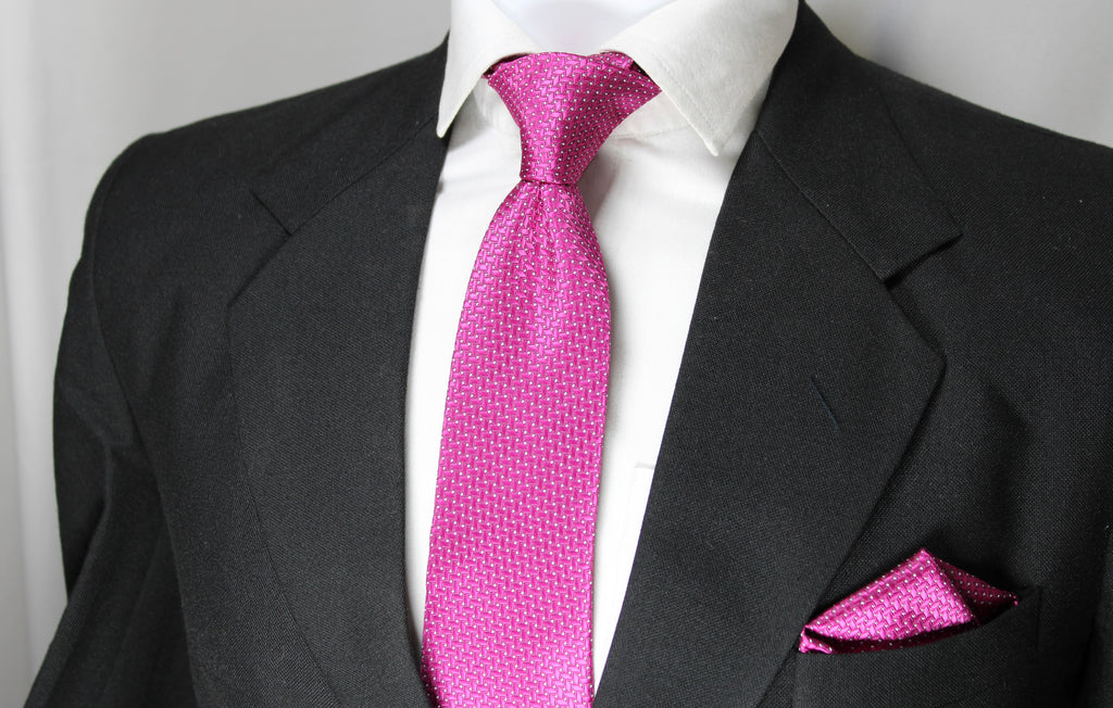 A set comprising a magenta necktie with a geometric pattern and a matching pocket square, displayed on a mannequin wearing a black suit and a white shirt.