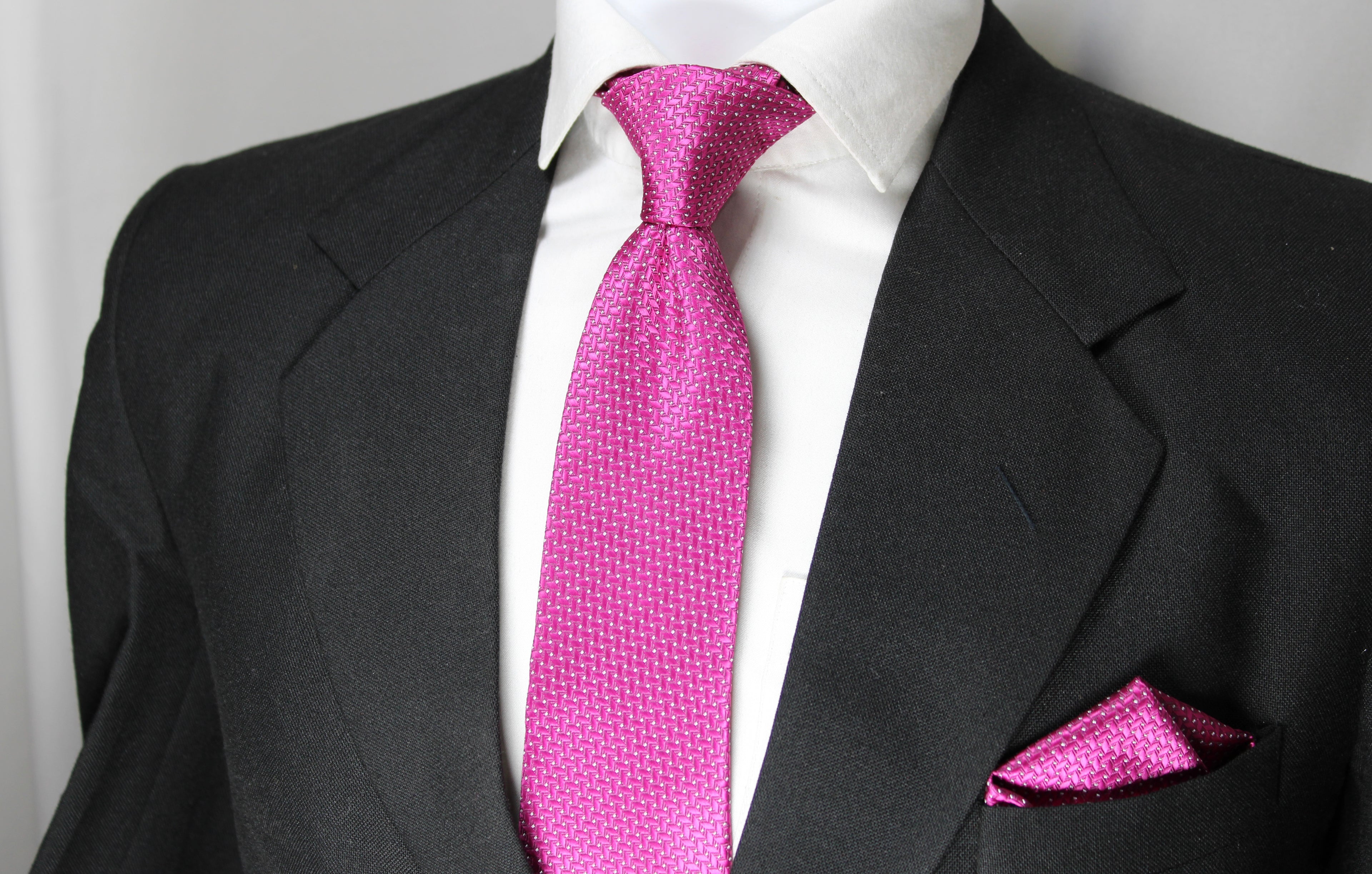 A set comprising a magenta necktie with a geometric pattern and a matching pocket square, displayed on a mannequin wearing a black suit and a white shirt.