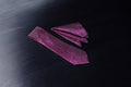 A set of magenta necktie and pocket square with a geometric pattern laid out on a dark surface.