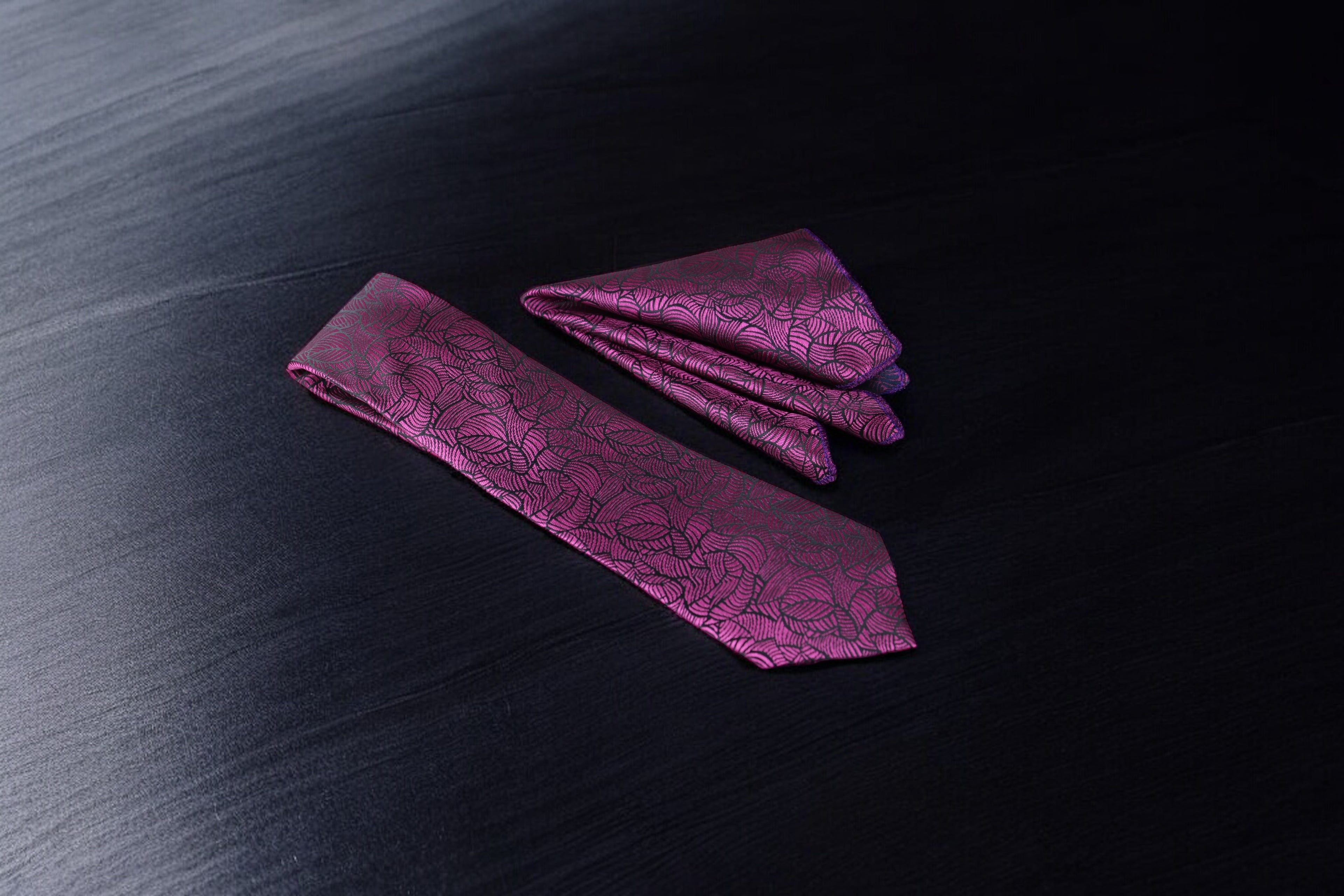 A set of magenta necktie and pocket square with a geometric pattern laid out on a dark surface.