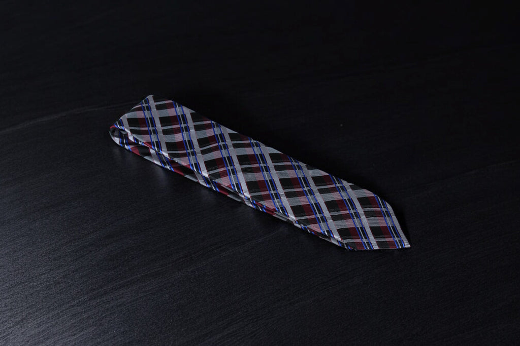 A checkered tie with maroon and black colors lying flat on a dark surface.