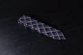 A checkered tie with maroon and black colors lying flat on a dark surface.