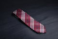 A checkered tie with maroon and navy colors laid out on a dark surface.