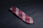 A checkered tie with maroon and navy colors laid out on a dark surface.