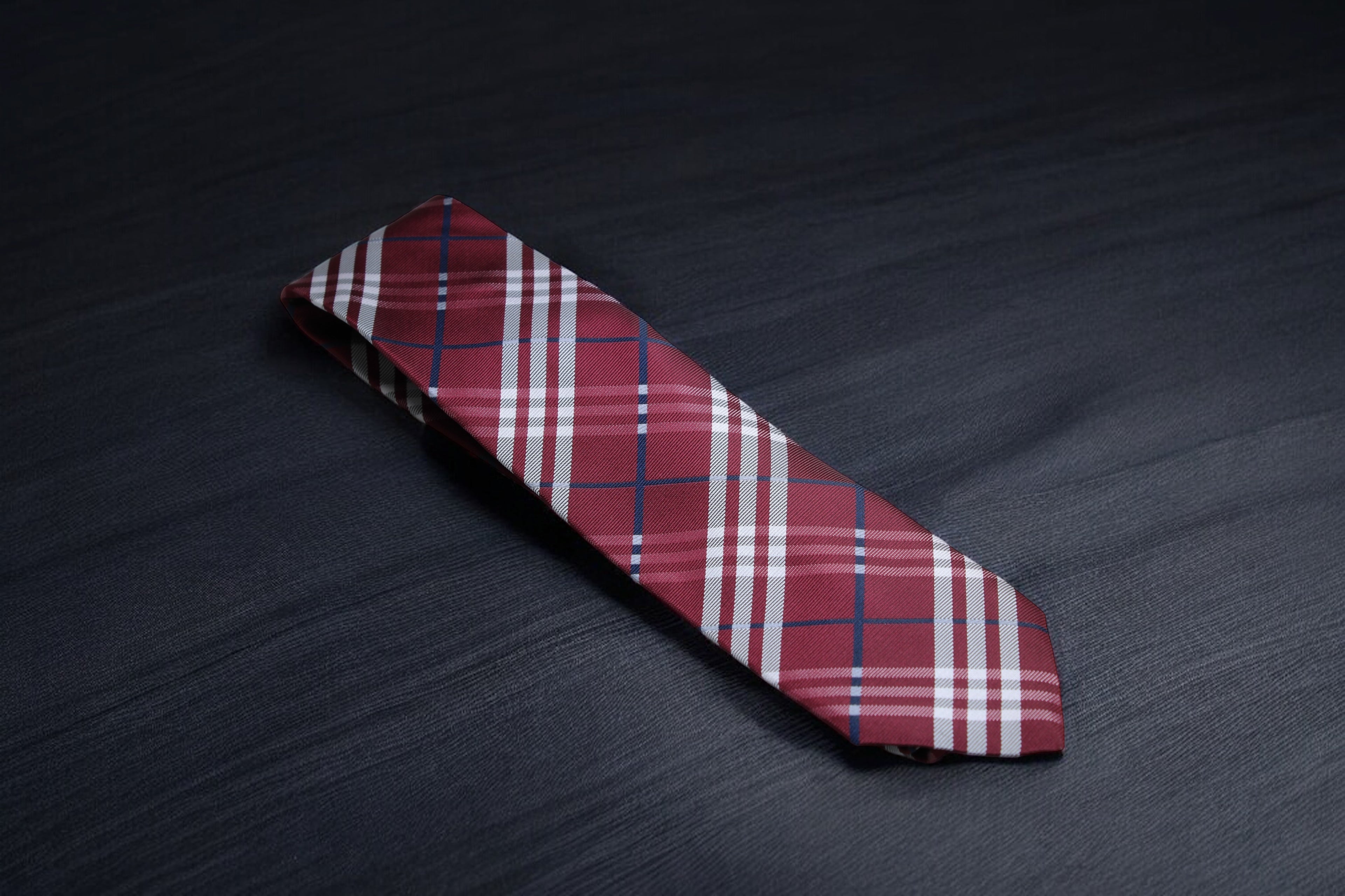A checkered tie with maroon and navy colors laid out on a dark surface.