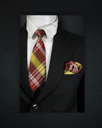 Black suit with a plaid red and yellow tie and matching pocket square on a dark background tie Bnon