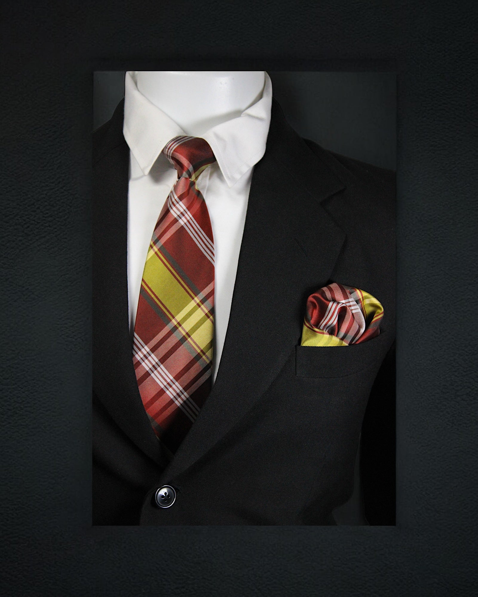 Black suit with a plaid red and yellow tie and matching pocket square on a dark background tie Bnon