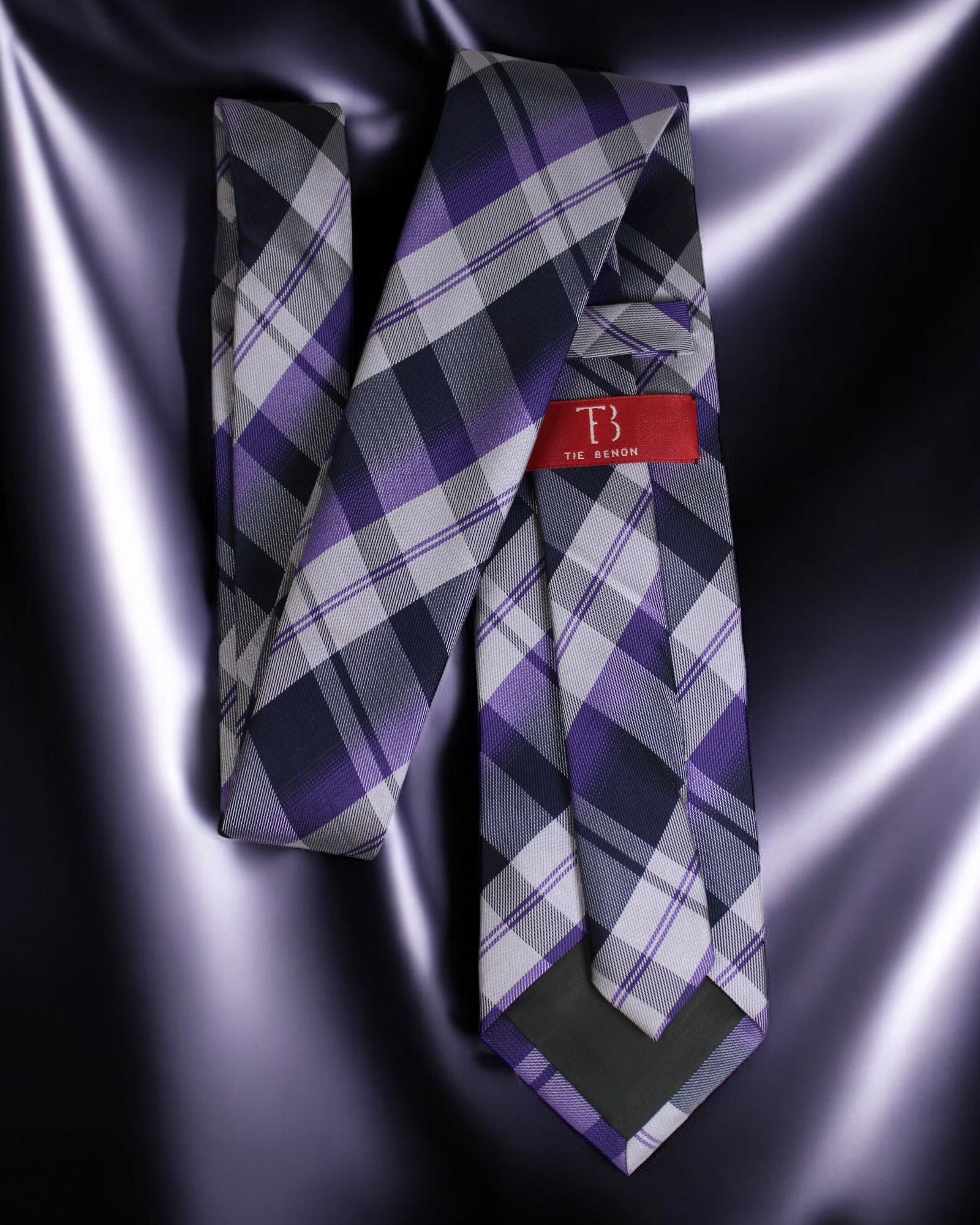 Purple and gray plaid tie with a red tag on a dark background