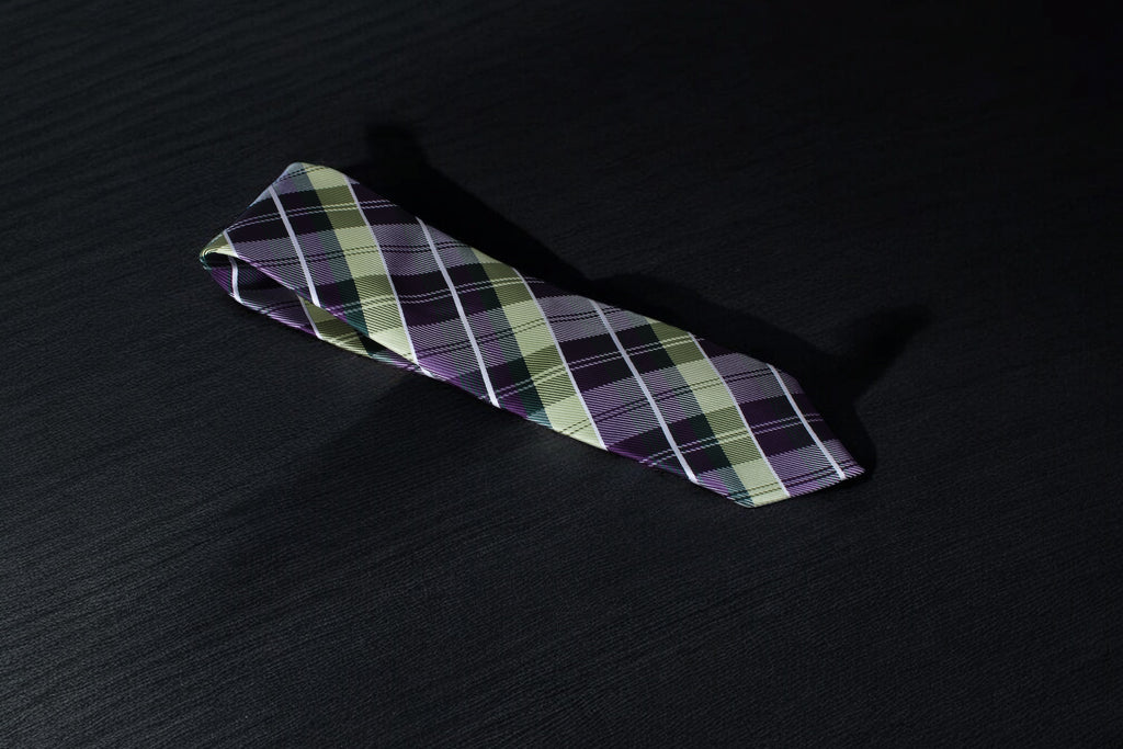 A purple and green checkered tie laid out on a dark surface.