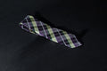 A purple and green checkered tie laid out on a dark surface.