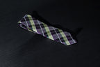 A purple and green checkered tie laid out on a dark surface.