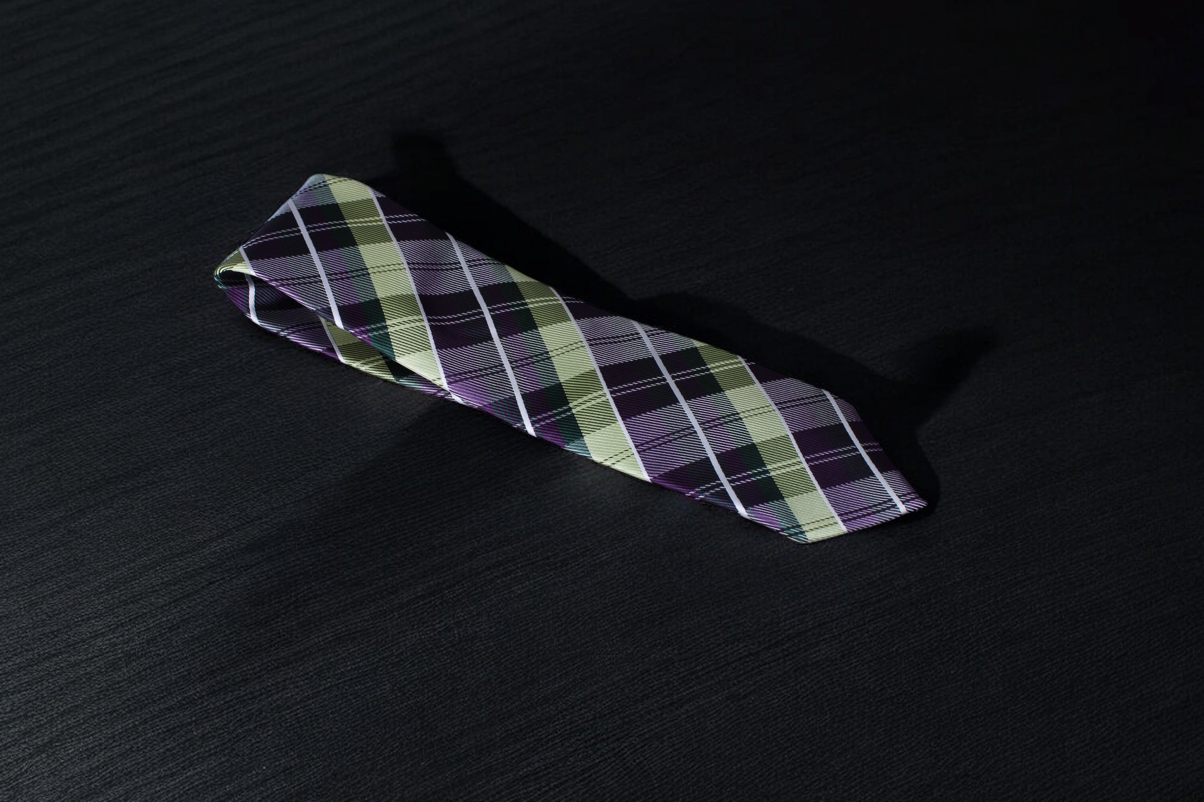 A purple and green checkered tie laid out on a dark surface.