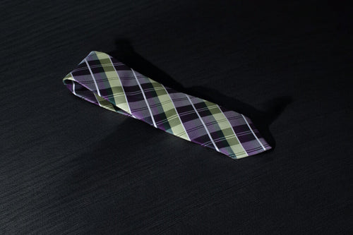 A purple and green checkered tie laid out on a dark surface.