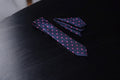 A navy and pink polka dotted tie and pocket square set laid out on a dark surface.