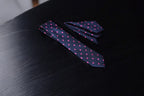 A navy and pink polka dotted tie and pocket square set laid out on a dark surface.