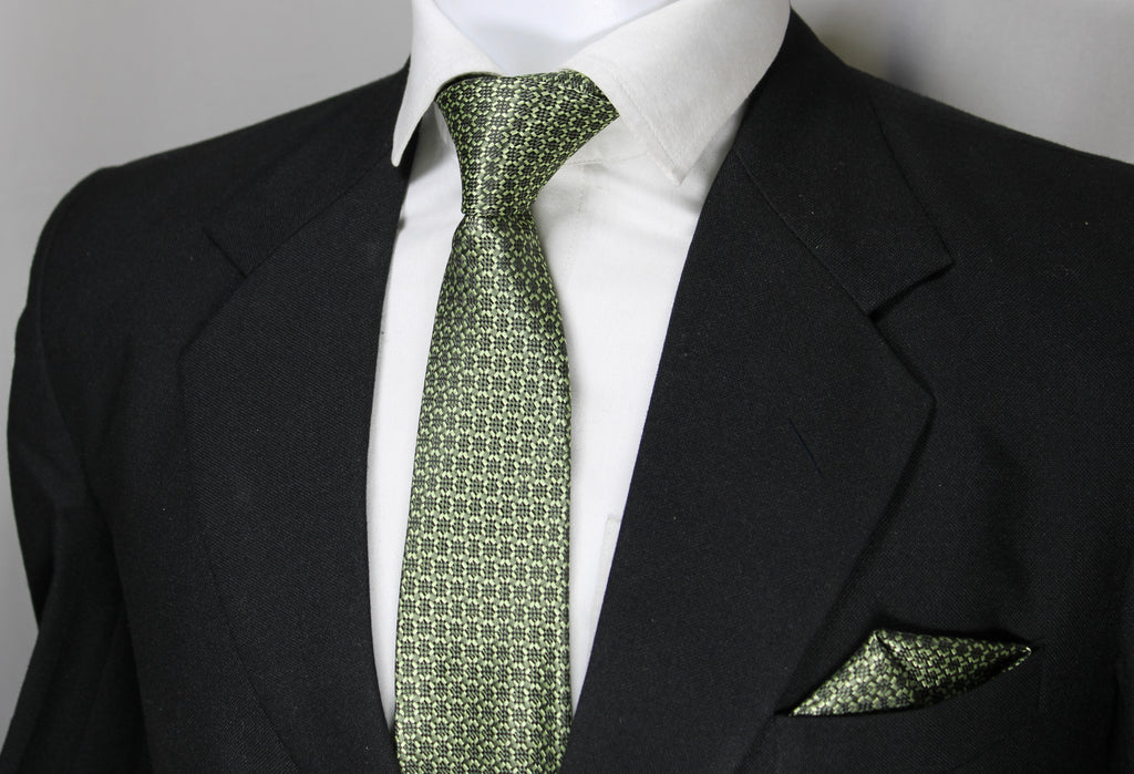 A set consisting of an olive green tie with a geometric pattern and a matching pocket square, displayed on a mannequin wearing a black suit and a white shirt.