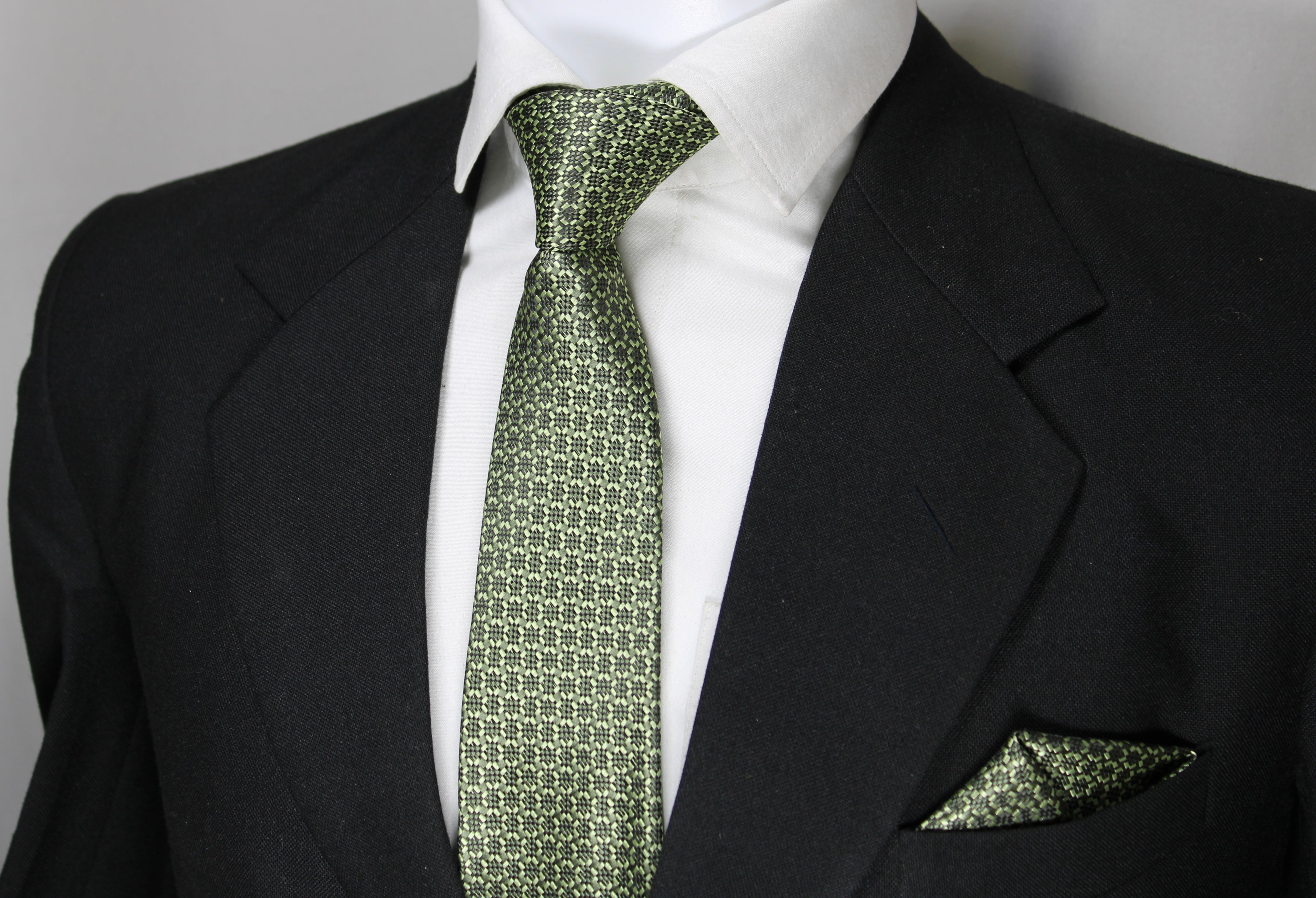A set consisting of an olive green tie with a geometric pattern and a matching pocket square, displayed on a mannequin wearing a black suit and a white shirt.
