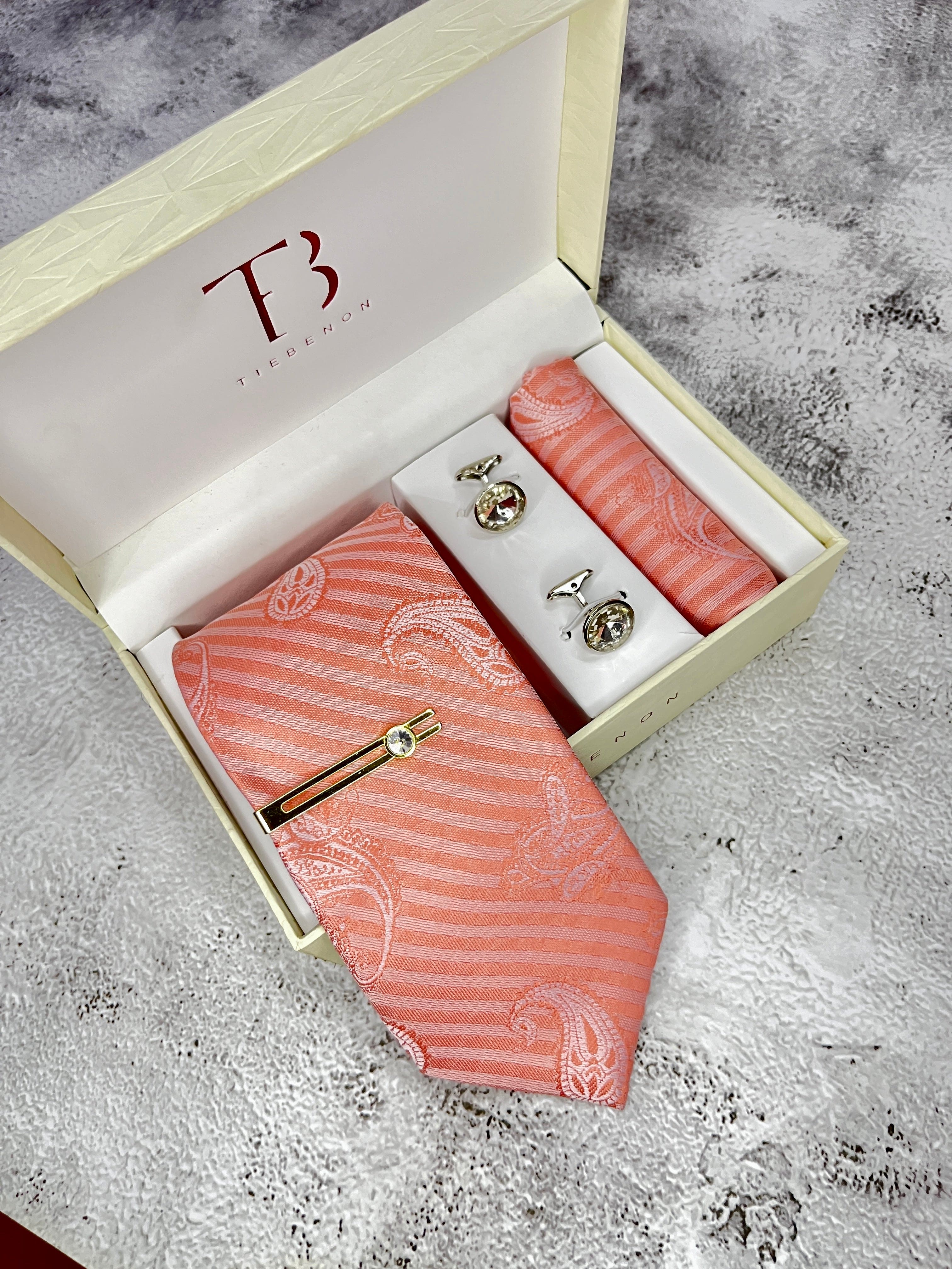 A peach colored tie with a subtle stripe pattern, accompanied by a matching pocket square and cufflinks, presented in an open white box with a 'T' logo on the top.