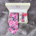 A Pink Floral Printed Silk Tie with a matching pocket square and a brass tie pin, presented in an open white box with a letter 'T' on the top and a pink rose flower on the side.