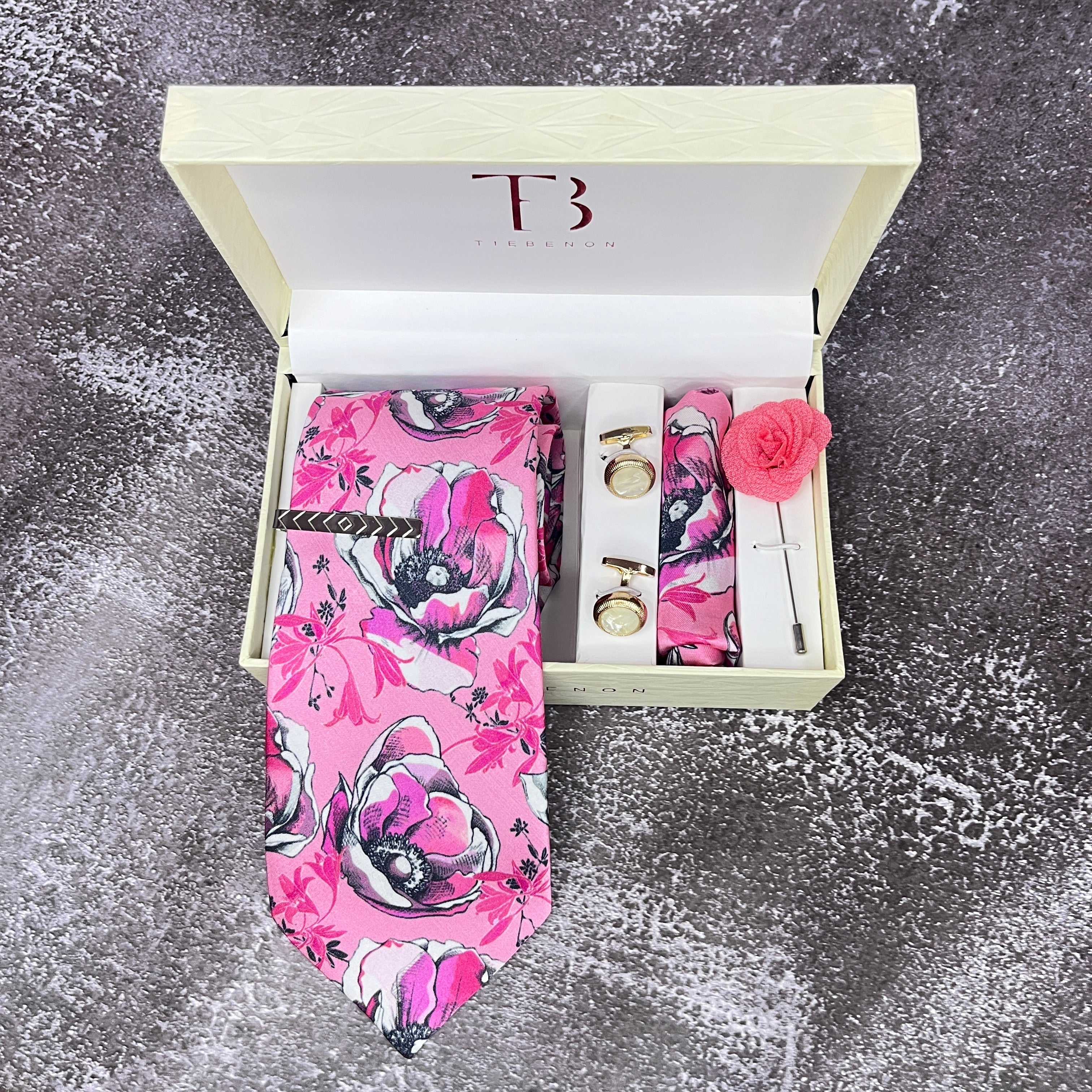 A Pink Floral Printed Silk Tie with a matching pocket square and a brass tie pin, presented in an open white box with a letter 'T' on the top and a pink rose flower on the side.
