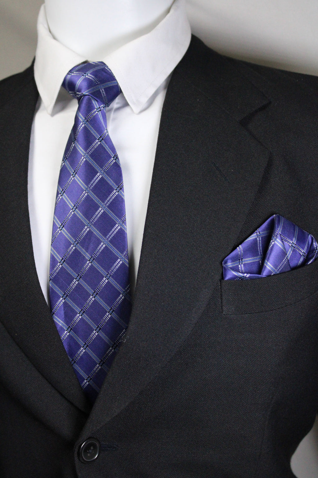 Close-up of a dark suit with a blue patterned tie and pocket square Tie Benon