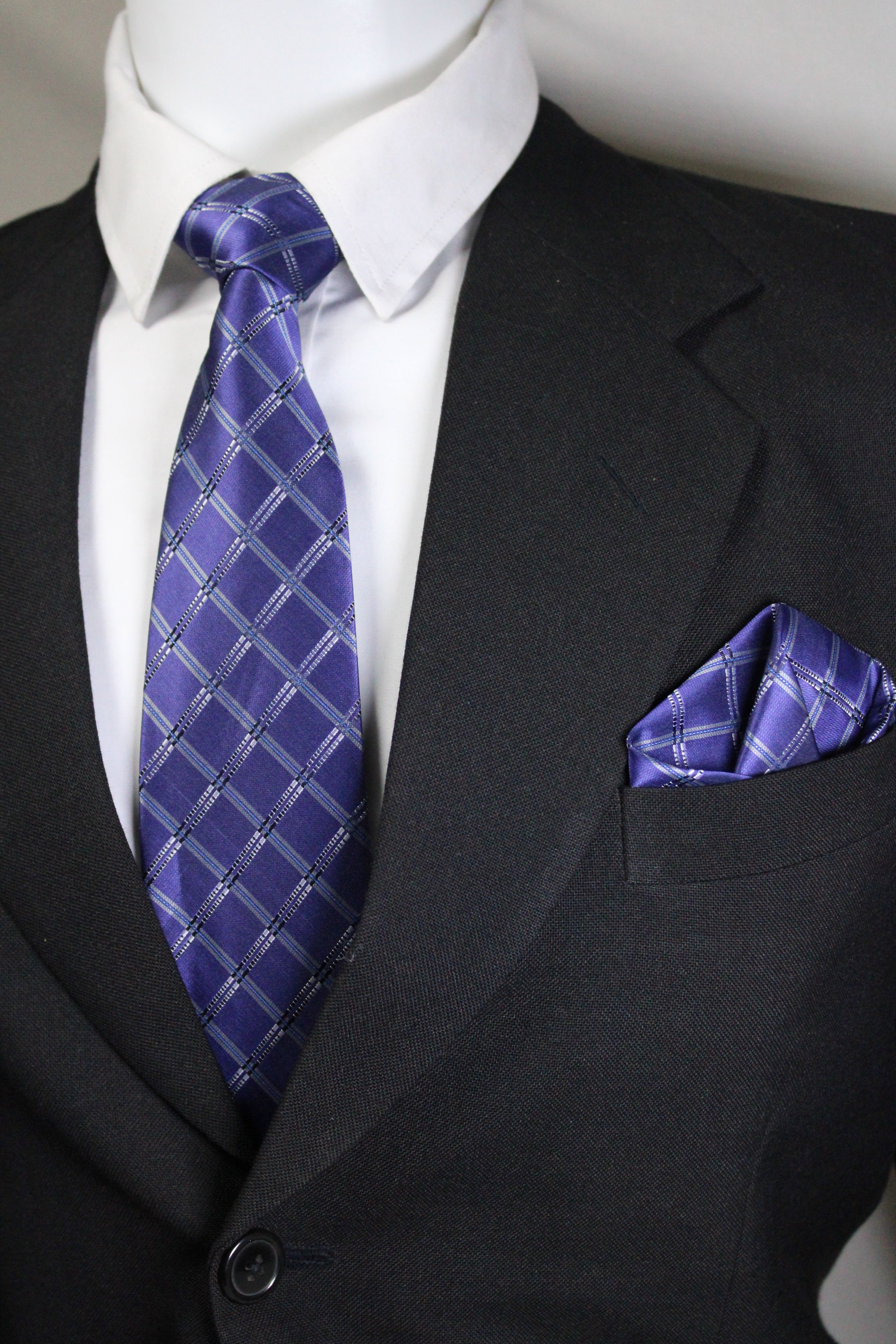 Close-up of a dark suit with a blue patterned tie and pocket square Tie Benon