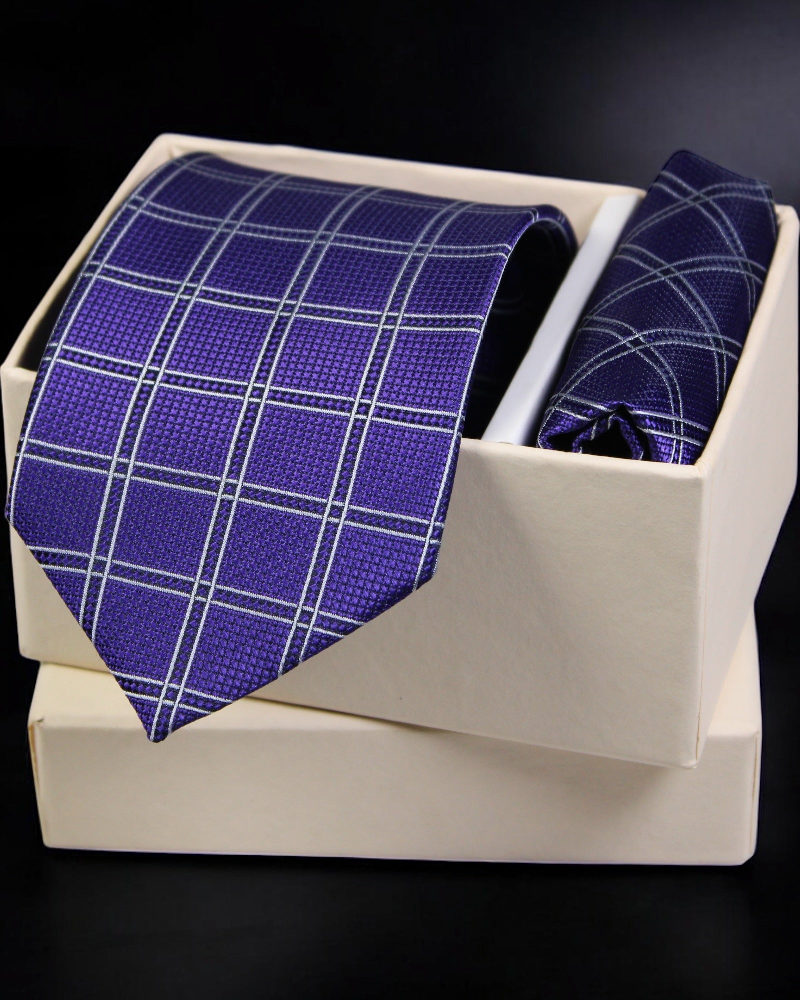 Blue checkered tie and pocket square set in a white box on a dark background tie benon