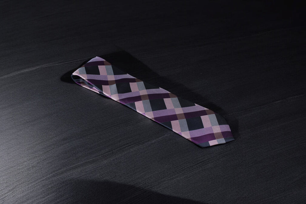 A purple and navy checkered tie laid out on a dark surface.