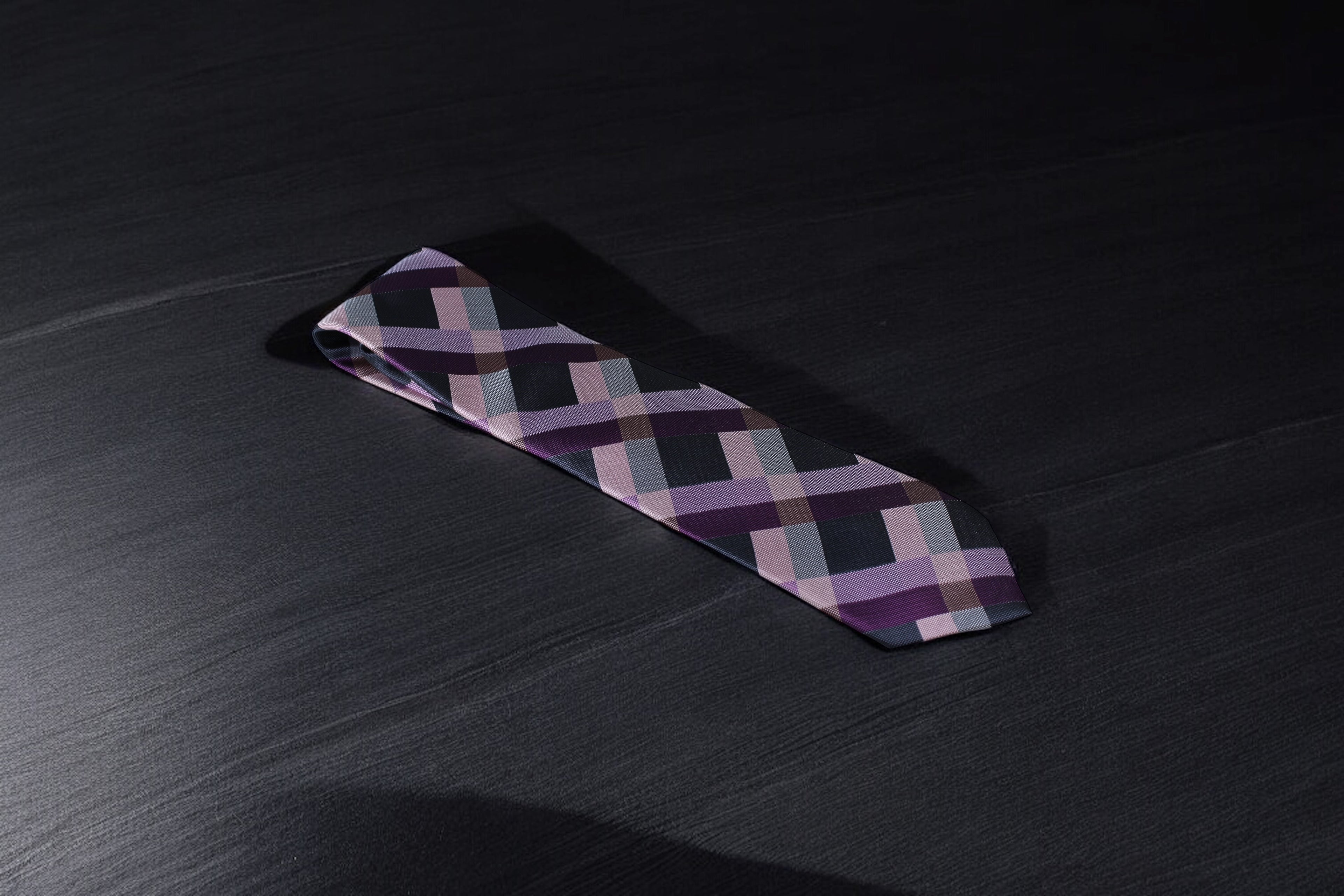 A purple and navy checkered tie laid out on a dark surface.