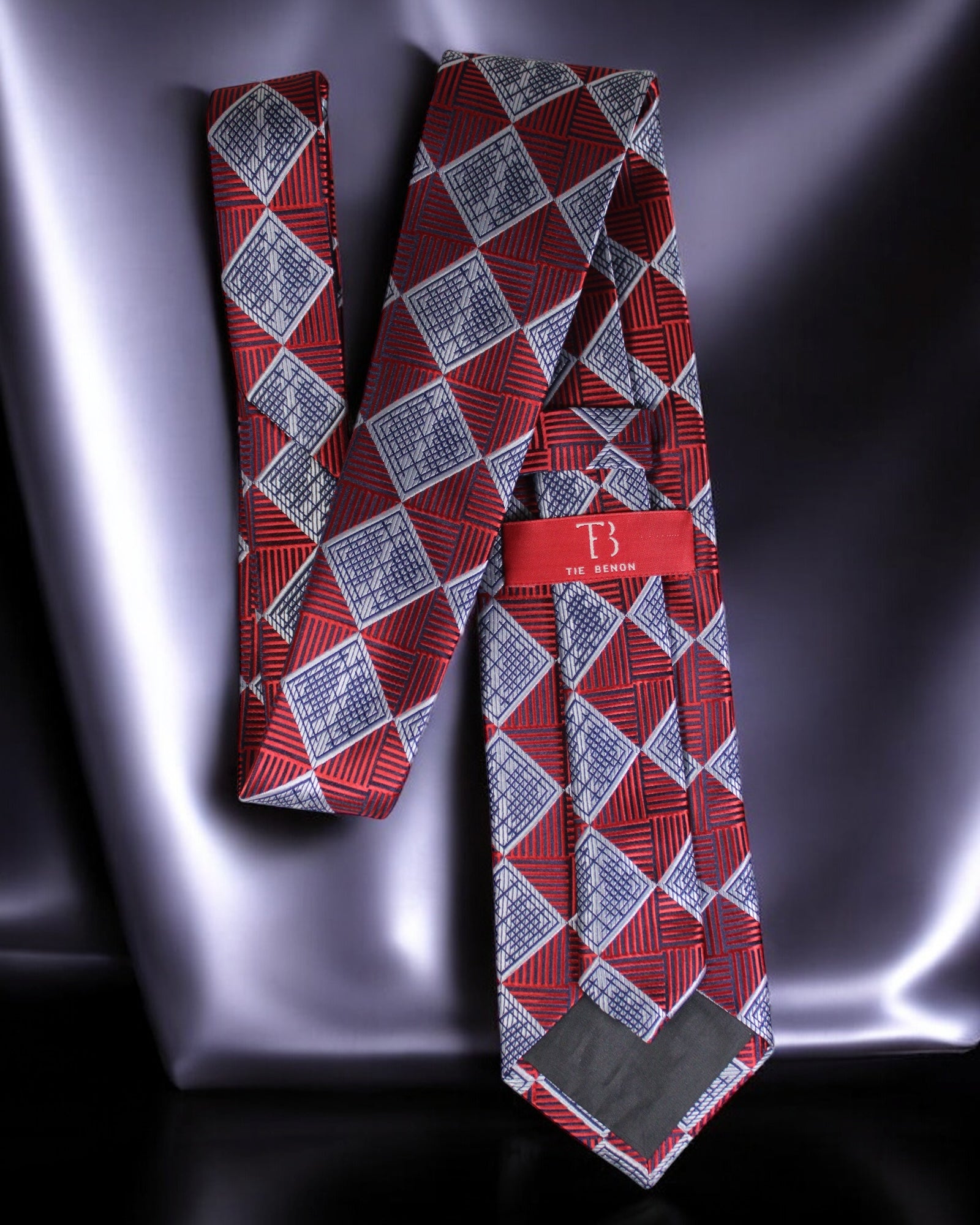 Red and gray patterned tie with a branded tag on a reflective surface Tie Benon