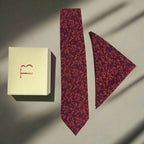 Red patterned tie and matching pocket square with a branded box on a neutral background